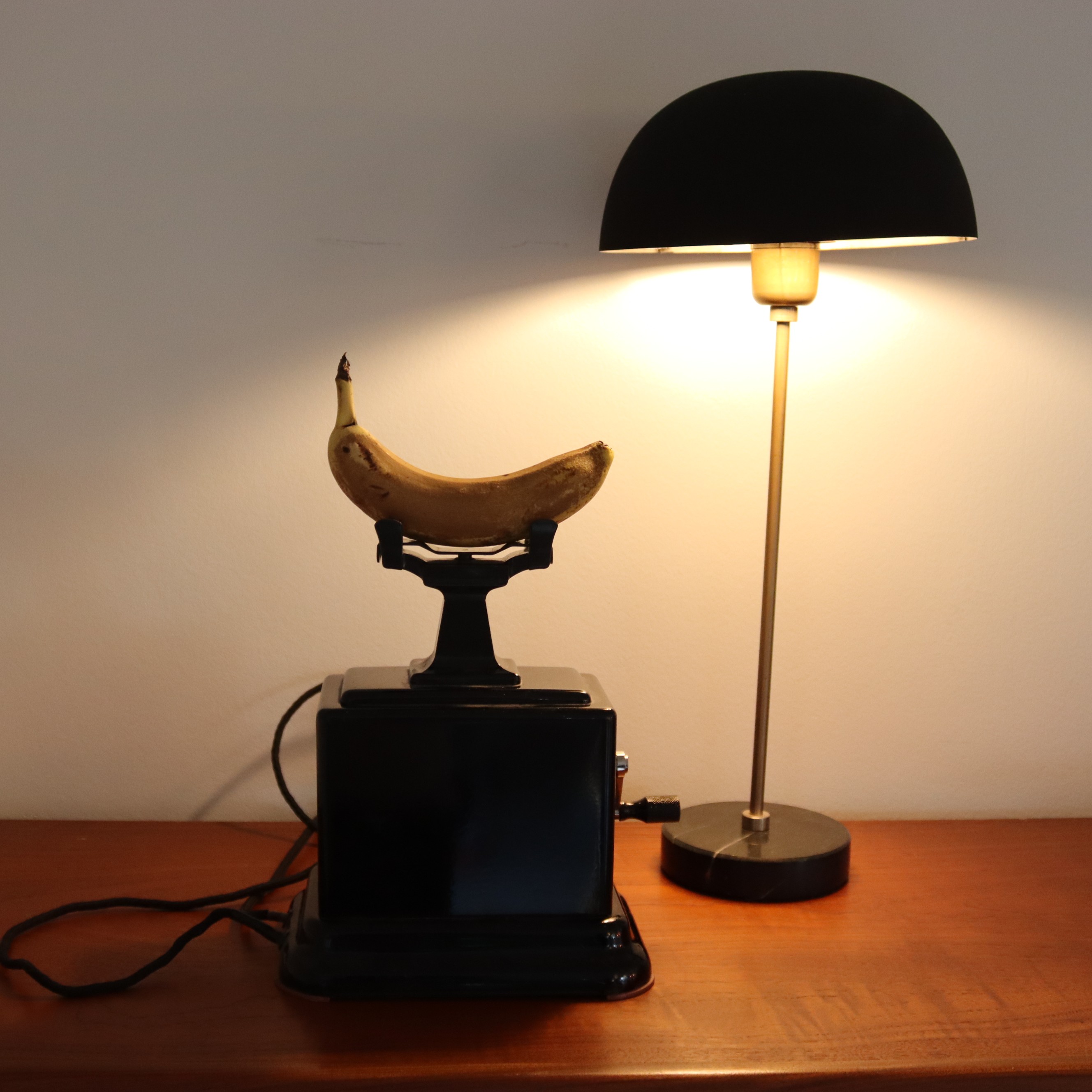 A banana resting on an antique telephone beside a lamp